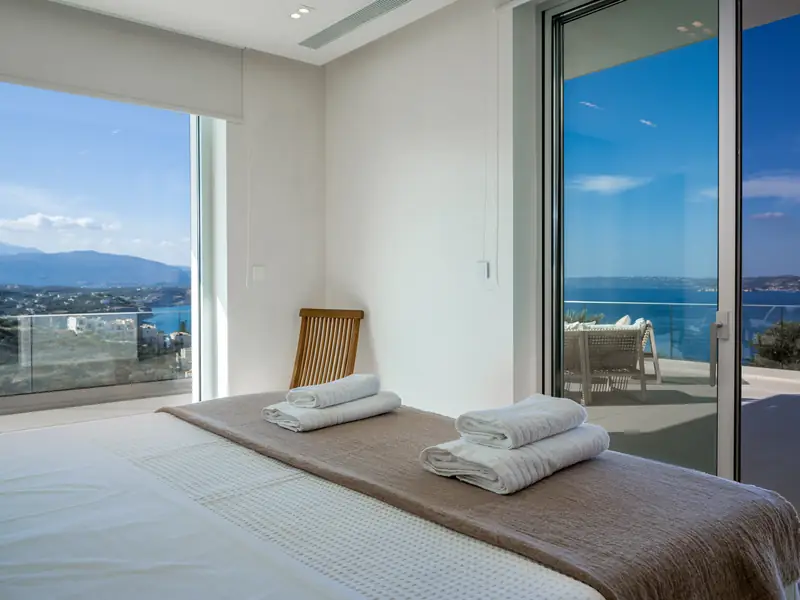 A bedroom with a glass wall and a view of the sea and the mountains