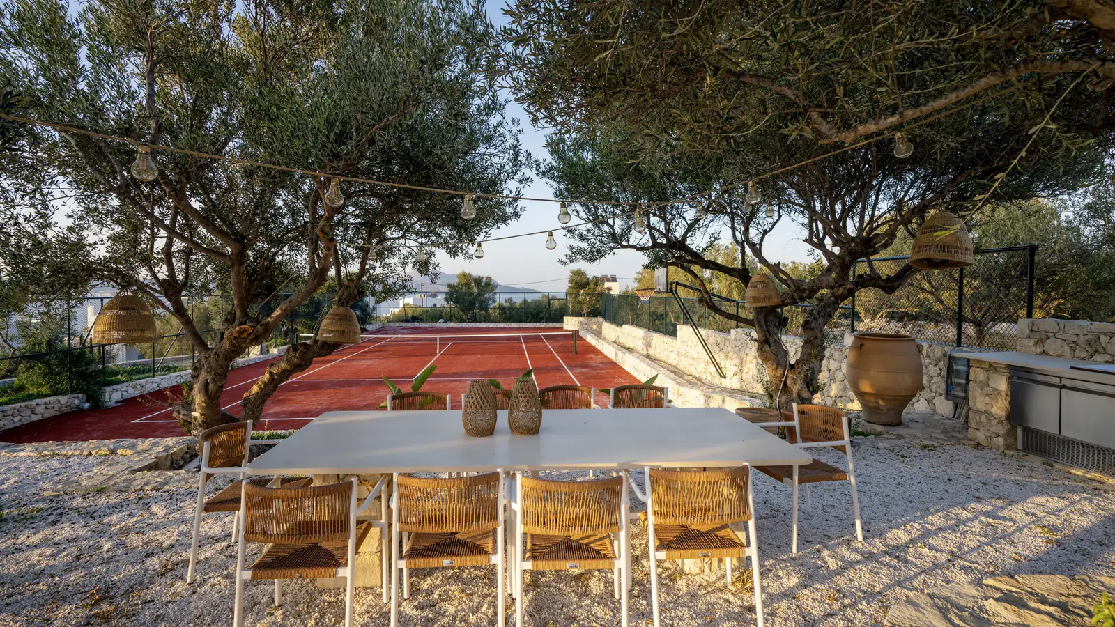 The long dining table under the olive trees, with the tennis court behind