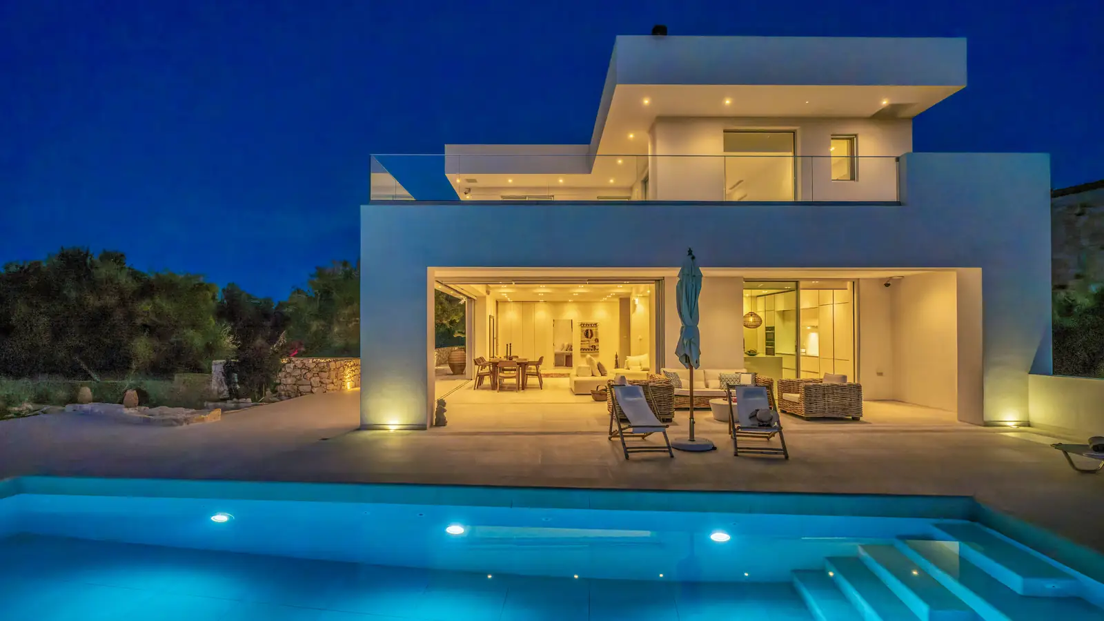 The house at dusk, with the lights on and the pool lit up