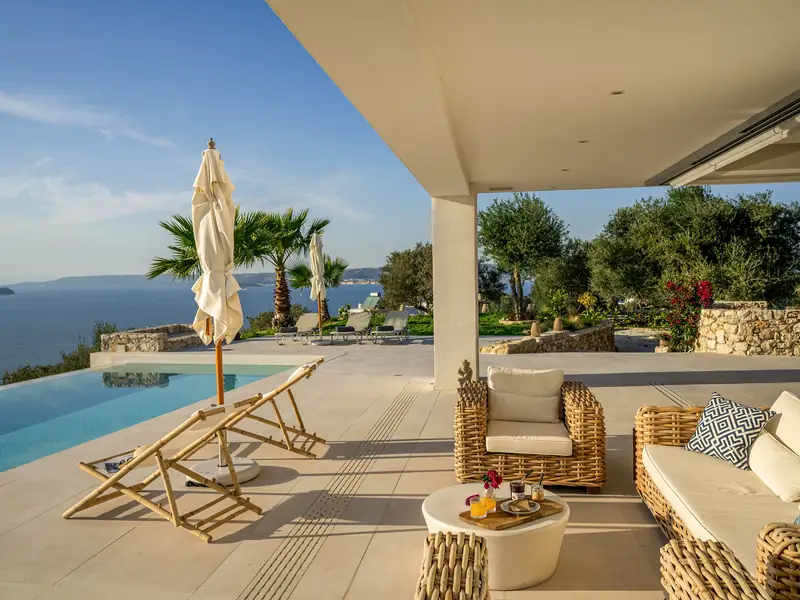 The pool terrace with sun loungers, a parasol and the sea